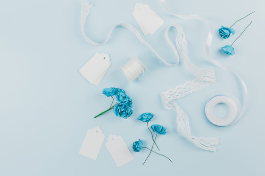 White tags; lace ribbon; spool and blue roses on colored background © Freepik