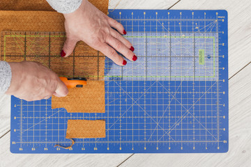 An overhead view of a woman's hand cutting fabric to smaller part with rotary cutter on wooden table