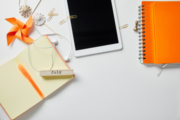 top view of digital tablet near orange notebooks, stationery, decoration objects and earphones on...