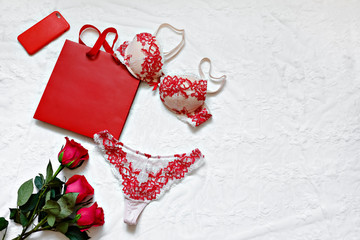 Red women's lingerie and red roses on white surface. Flat lay. Copy space. Gift Concept. Romantic evening.