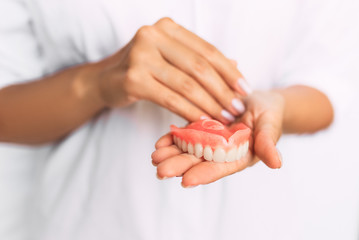 The dentist is holding dentures in his hands. Dental prosthesis in the hands of the doctor close-up. Dentistry conceptual photo. Prosthetic dentistry. False teeth. Removable denture - obrazy, fototapety, plakaty