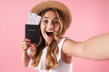 Young pretty woman posing isolated over pink wall background holding passport with tickets take a...