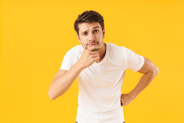 Photo of thoughtful man in basic t-shirt touching his chin and looking at camera with pensive face