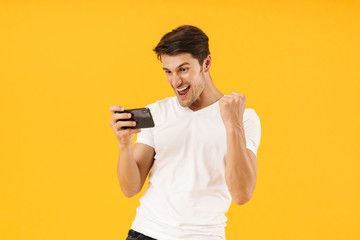 Photo of happy man in basic t-shirt rejoicing while playing video game on smartphone