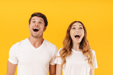 Portrait of delighted couple man and woman in basic t-shirts wondering with open mouthes while...