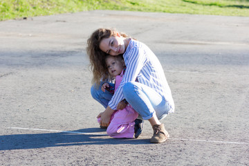 Happy young woman sitting  on road and hugging  little girl