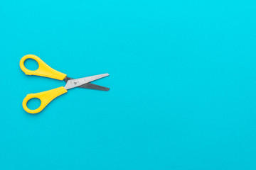 minimalist photo of yellow children's scissors on the turquoise blue background. flat lay shot of opened yellow scissors with copy space