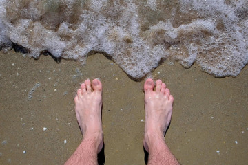Man stands barefeet on sandy beach on warm Sunny day. Waves roll back and forth. Concept of...