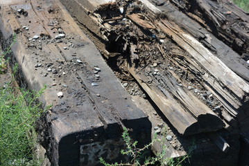Old black and brown wooden bars from the railway line, broken and cracked by time. Very unique wooden background with unusual color under sunlight.