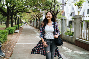 asian young woman tourists walking on pathway in park in Barcelona Spain. beautiful smiling lady backpacker relax in spring weather with sunshine outdoor. girl leave church going home on the way.