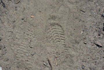 Imprint of men's shoes on the gray sand in sunny light.