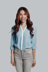 Portrait of confidence. Attractive young woman looking at camera and smiling while standing against grey background