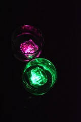 Multicolored glowing ice cubes float in a crystal champagne glass that illuminates the drink in it.