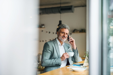 Mature man with coffee and smartphone at the table in a cafe.
