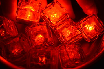 Plastic glowing bright red ice cubes in water. Red ice floes are floating in a stainless steel dipper with an interesting metal reflection. Red water background with red spot lighting.