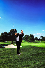 Mann im Business Anzug, stehend auf einer Bergwiese mit Golfschläger