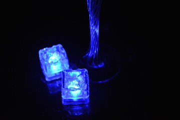 Multicolored glowing ice cubes float in a crystal champagne glass that illuminates the drink in it.