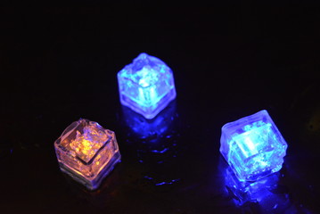 Beautiful plastic glowing ice cubes on a glossy black background. Resting diode lighting blue and...
