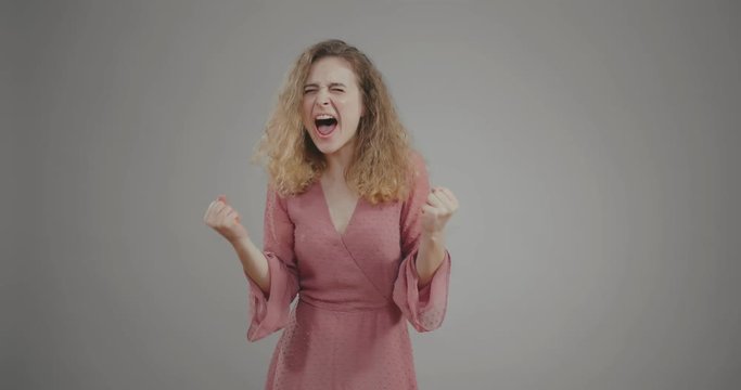 Pretty girl rejoices and screams out of joy on grey background