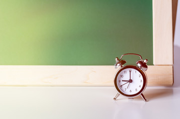 Back to school. Alarm clock on the background of the school board. School background with space for your text.