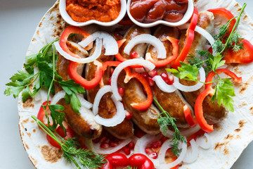 Fried pork sausages on pita bread with ketchup and Armenian appetizer Aivar with vegetables. Lavash, red bell pepper, onions, sausages. Oktoberfest food, the concept of the pub