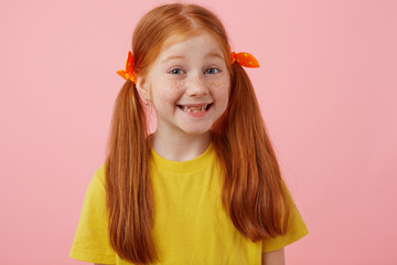 Close up of happy petite freckles red-haired girl with two tails, broadly smiling and looks cute,...
