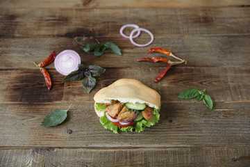 Pita - sandwich, sabiche stuffed with chicken, tomatoes, cucumbers, salad on a wooden rustic background decorated with vegetables and pepper. Middle Eastern cuisine. With copy space for text.