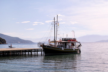 Tourist boat cruiser in small marina on sea and beautiful beach, waiting tourists for ship is sailing out of port for next tourist tour. Anchored cruise ship in harbor. Summer season, travel, holiday.