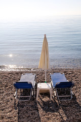 Early morning on sandy beach without people with empty chaise lounges, sun beds, sunshades, summer umbrella parasol, deck chairs, table, loungers for sunbathing on ocean beach waiting for tourists.