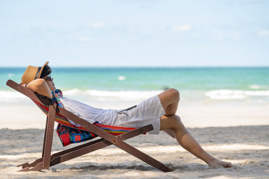 Young asian adult men traveler in casual wear and sun glass relaxing and lying  down on colorful beach chair on tropical island beach in summer holidays  vacation travel trip with smartphone. Stock Photo | Adobe Stock