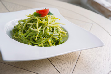 green spinach spaghetti with cheese and tomato on wooden table