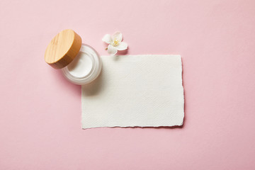 top view of open jar with wooden cap, piece of paper and jasmine flower on pink