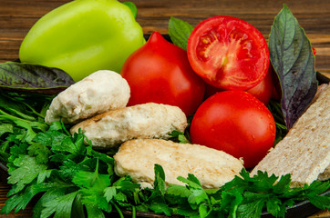 Steamed white meat cutlets on a platter and parsley substrate, surrounded by tomatoes, basil leaves and sweet pepper.