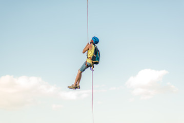 Happy successful rock climber hanging on rope
