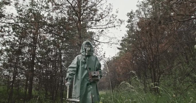 Man in WWII Hazmat suit and gas mask using a probe and counter to test forest vegetation for chemical contamination. RAW video recrod.