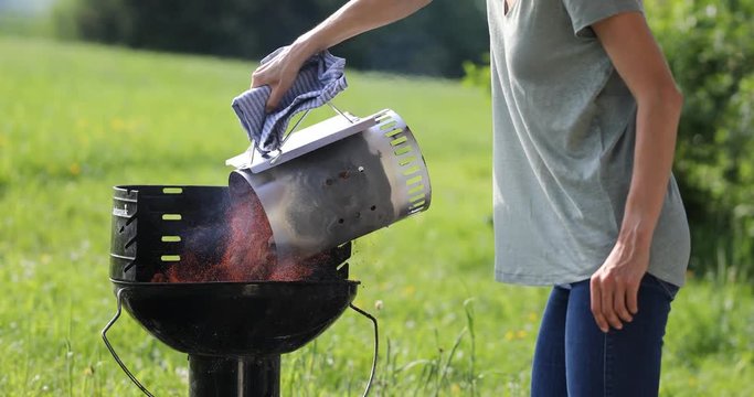 Woman pouring preheated charcoal onto grill for barbecue