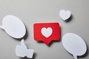 red like card, speech bubbles, thumbs up and small paper heart on white surface