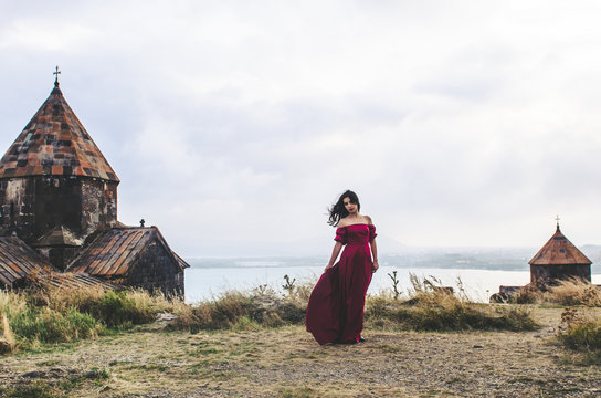Portrait of young woman in red dress standing near monastery, Armenia