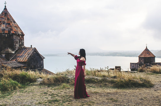 Portrait of young woman in red dress standing near monastery, Armenia