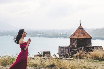 Portrait of young woman in red dress standing near monastery and pray, Armenia