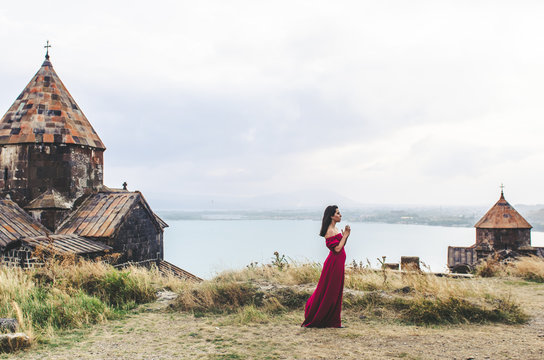 Portrait of young woman in red dress standing near monastery and pray, Armenia