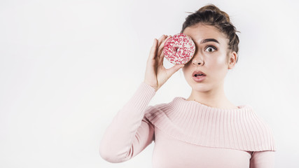 Shocked young woman pout her lips covering the eyes with donut on white backdrop