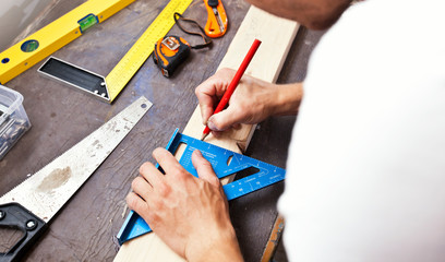 The carpenter is draw the line by pencil on the wooden plank