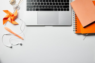 top view of orange notepads, earphones, pen and laptop on white surface