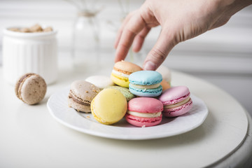 Close-up of hand picking up the colorful macaroons from white plate on the table