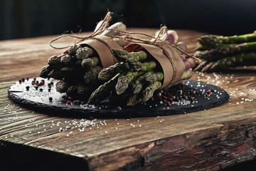 An edible, raw stems of asparagus on a wooden background.