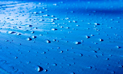 Large drops of water on a blue textile with a waterproof effect. Water-repellent impregnation. Texture drops on the fabric. Selective focus