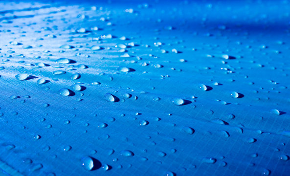 Large Drops Of Water On A Blue Textile With A Waterproof Effect. Water-repellent Impregnation. Texture Drops On The Fabric. Selective Focus