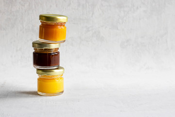 Three Small glass jar with metal cap with light yellow, orange and dark brown honey one on another isolate on grey cement background with copy space. Healthy product, natural, Horizontal