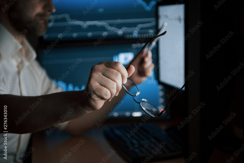 Poster close up view. bearded man in white shirt holds glasses in the office with multiple computer screens